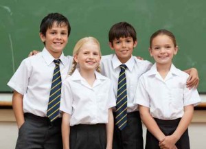 Smiling schoolfellows in school uniforms standing in front of bl